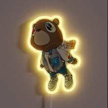 Load image into Gallery viewer, Neon sign of a cartoon bear wearing a varsity jacket and sneakers, floating with a graduation cap and backpack, glowing with a yellow outline
