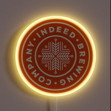 Load image into Gallery viewer, indeed-brewing-company-yellowpop-93558 – Round neon sign with an orange background and white snowflake-style logo for Indeed Brewing Company, outlined in soft yellow glow